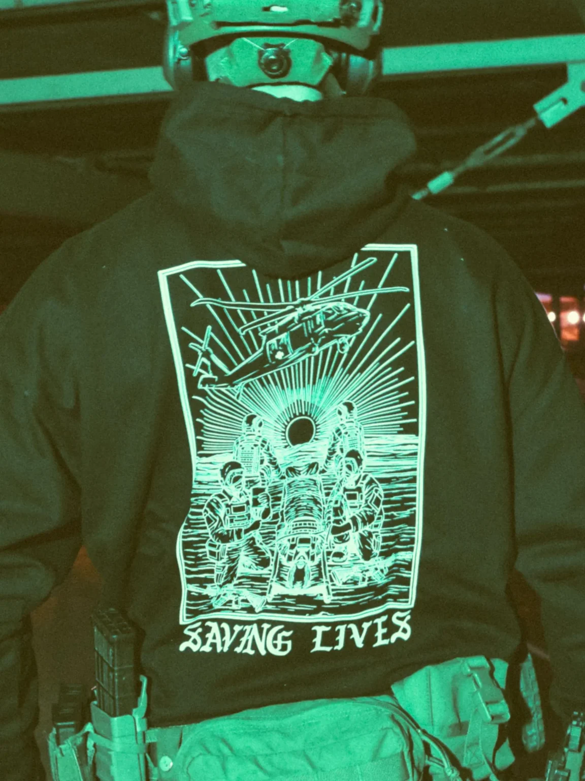 Military-style hoodie featuring the Saving Lives design: a group of soldiers carrying a stretcher while a helicopter prepares to land, symbolizing courage under pressure.