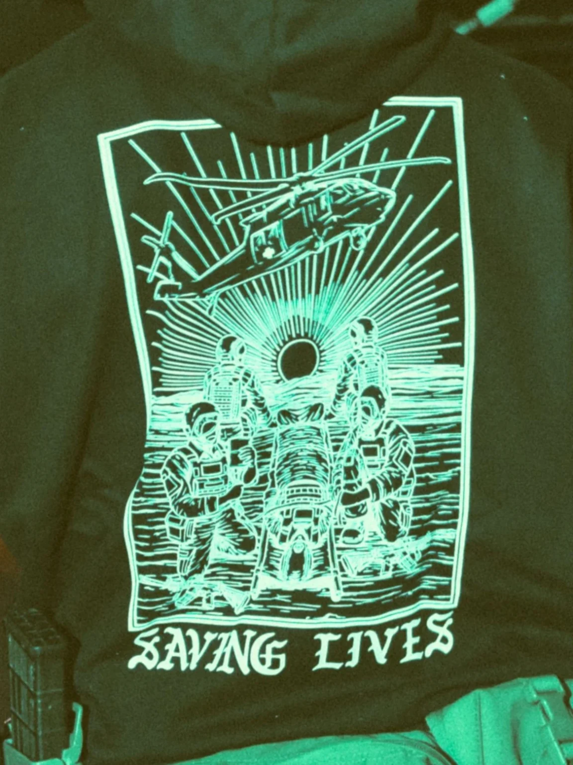 Military-style hoodie featuring the Saving Lives design: a group of soldiers carrying a stretcher while a helicopter prepares to land, symbolizing courage under pressure.