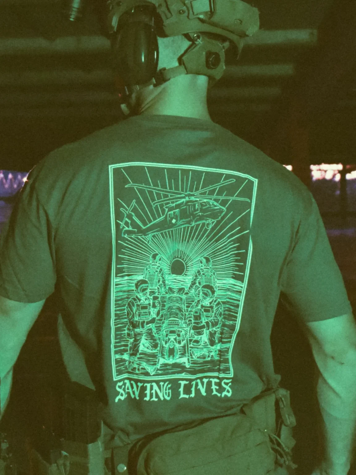 Cotton T-shirt with Saving Lives artwork showing soldiers in action, holding a stretcher during a tense medevac moment with a helicopter descending nearby.