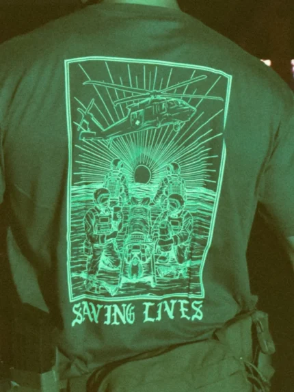 Cotton T-shirt with Saving Lives artwork showing soldiers in action, holding a stretcher during a tense medevac moment with a helicopter descending nearby.