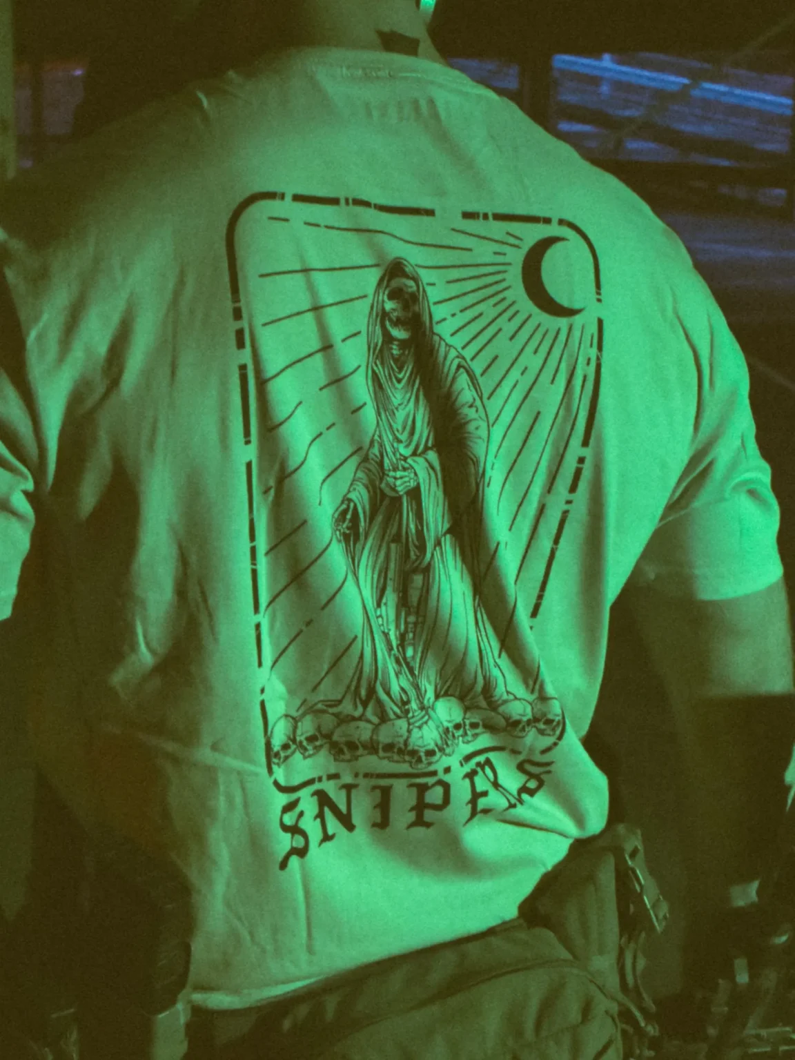Tactical T-shirt with a skeletal sniper design, positioned on a pile of skulls and holding a high-caliber Arctic Warfare Super Magnum rifle.
